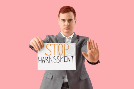 Joven empresario sosteniendo papel con texto STOP HARASSMENT sobre fondo rosa