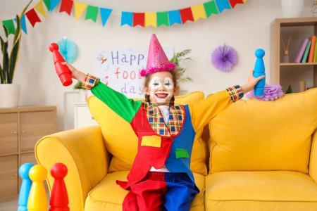 Funny little girl in clown costume with juggling clubs at home. April Fools' Day celebration