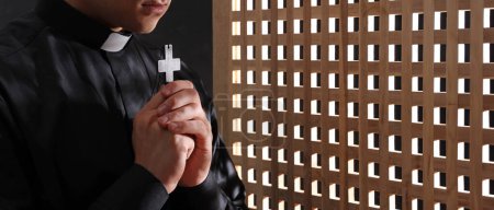 Joven sacerdote con cruz en cabina de confesión, primer plano