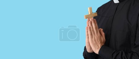 Junger Priester hält Kreuz auf hellblauem Hintergrund mit Platz für Text, Nahaufnahme