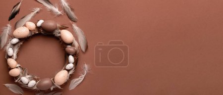 Photo for Easter wreath and feathers on brown background with space for text, top view - Royalty Free Image
