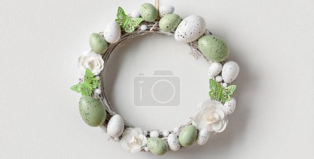 Photo for Easter wreath made of flowers, eggs and butterflies hanging on white wall - Royalty Free Image
