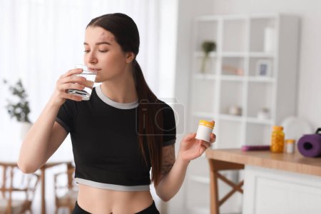 Mujer joven deportiva con botella de suplementos vitamínicos beber agua en casa