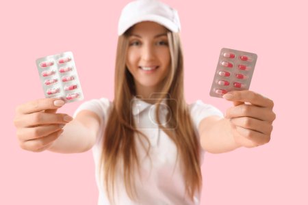 Beautiful woman with blisters of vitamin supplements on pink background, closeup