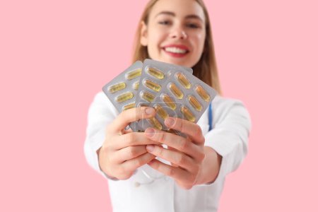 Schöne Ärztin mit Blasen von Vitaminpräparaten auf rosa Hintergrund, Nahaufnahme
