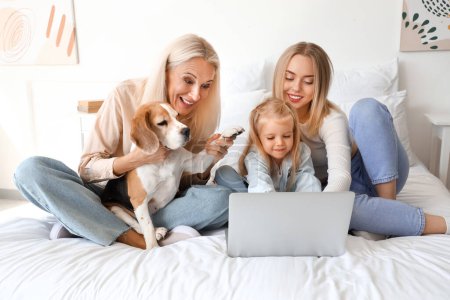 Famille heureuse avec chien mignon en utilisant un ordinateur portable dans la chambre