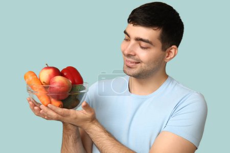 Young man with bowl of food rich in vitamin A on blue background