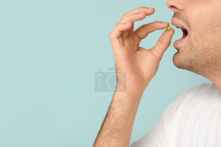 Young man with taking vitamin A pill on blue background, closeup