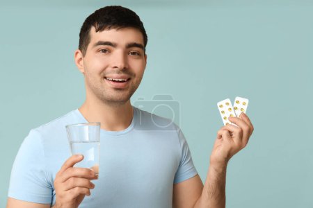 Foto de Hombre joven con ampollas de píldoras de vitamina A y agua sobre fondo azul, primer plano - Imagen libre de derechos