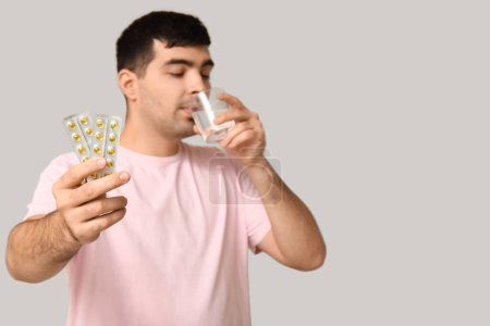 Foto de Hombre joven con ampollas de píldoras de vitamina A beber agua sobre fondo claro, primer plano - Imagen libre de derechos