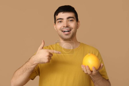 Young man pointing at grapefruit rich in vitamin A on beige background