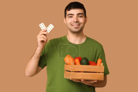 Junger Mann mit Blasen von Vitamin-A-Pillen und gesunder Ernährung auf beigem Hintergrund
