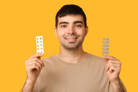 Foto de Hombre joven con ampollas de píldoras de vitamina A sobre fondo amarillo, primer plano - Imagen libre de derechos