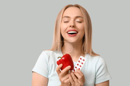 Junge Frau mit Vitamin-A-Pillen und Paprika auf hellem Hintergrund