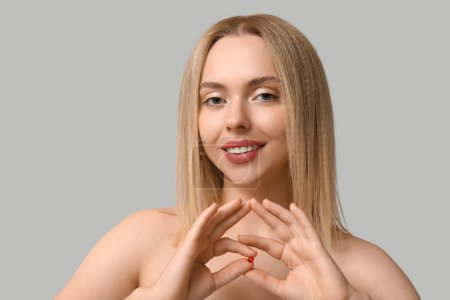 Young woman with vitamin A pills on light background