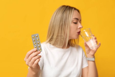 Photo for Young woman with vitamin A pills and glass of water on yellow background, closeup - Royalty Free Image