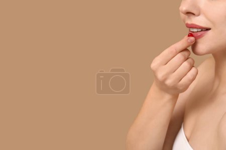 Junge Frau nimmt Vitamin-A-Pille auf beigem Hintergrund, Nahaufnahme