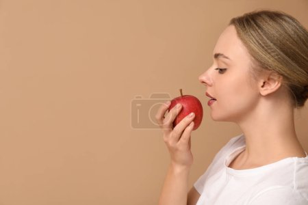 Junge Frau mit Apfel auf beigem Hintergrund, Nahaufnahme