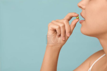 Hübsche junge Frau nimmt Vitamin-A-Kapsel auf blauem Hintergrund, Nahaufnahme