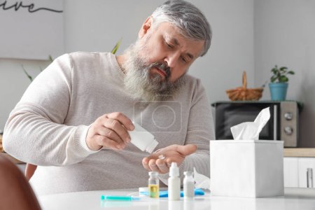 Portrait of sad senior man sitting at table with tissues and medicine in kitchen