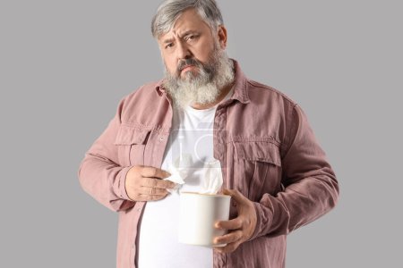 Portrait of sad senior man with tissues on grey background