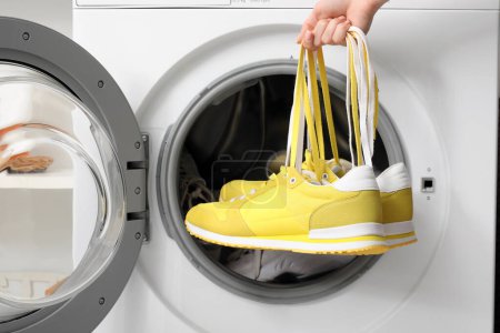 Female hands with sneakers and open washing machine, closeup