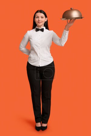 Téléchargez les photos : Belle jeune serveuse avec plateau et cloche sur fond orange - en image libre de droit
