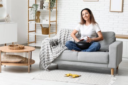 Happy mature woman with glucophone on sofa at home