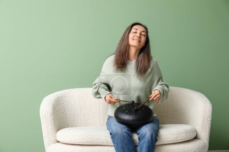 Schöne reife Frau mit Stöcken spielt glukophonisch auf dem Sofa vor grünem Hintergrund