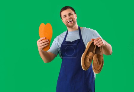 Male shoemaker with insoles and shoes on green background