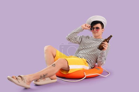 Photo for Young sailor with beer sitting on ring buoy against lilac background - Royalty Free Image