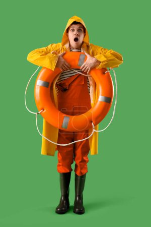 Photo for Shocked young sailor in raincoat with ring buoy on green background - Royalty Free Image