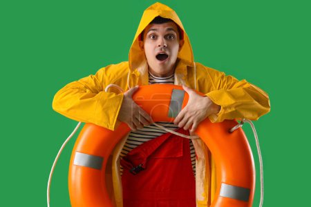 Photo for Shocked young sailor in raincoat with ring buoy on green background - Royalty Free Image