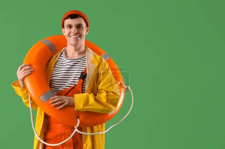 Young sailor in raincoat with ring buoy on green background