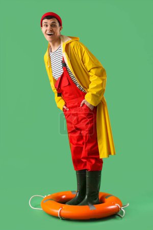 Photo for Young sailor in raincoat with ring buoy on green background - Royalty Free Image
