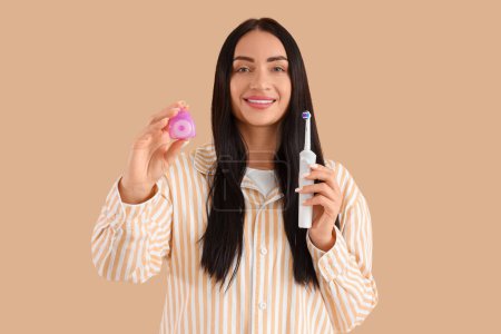 Téléchargez les photos : Belle jeune femme heureuse avec fil dentaire et brosse à dents électrique sur fond beige - en image libre de droit