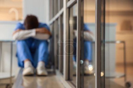 Infirmière masculine stressée assise sur le rebord de la fenêtre à l'hôpital le soir, gros plan
