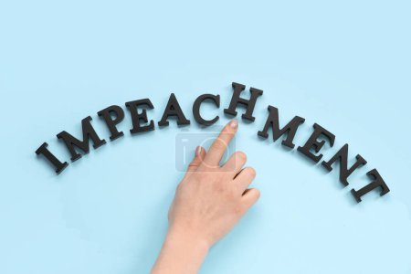 Female hand with black letters spelling word IMPEACHMENT on blue background