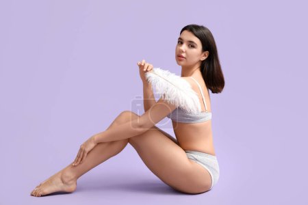 Beautiful young woman with soft feather sitting against lilac background. Epilation concept