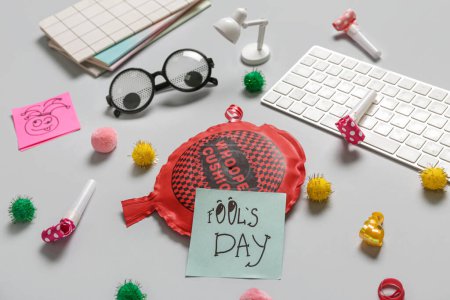 Computer keyboard with whoopee cushion, funny glasses and sticky notes on white background. April Fools Day prank