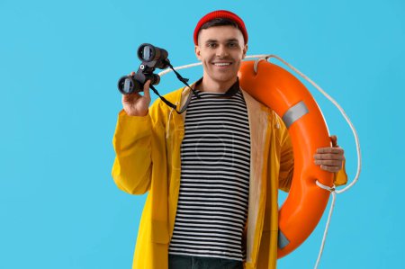 Photo for Young sailor with ring buoy and binoculars on blue background - Royalty Free Image