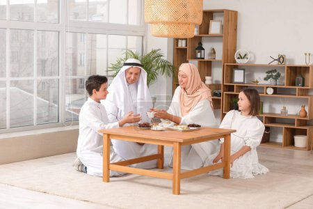Glückliche muslimische Familie am Tisch mit traditionellen Süßigkeiten im Wohnzimmer. Eid al-Fitr-Feier