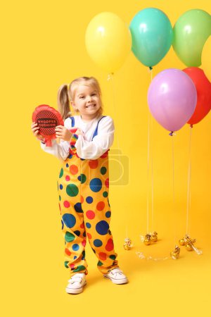 Cute little girl with whoopee cushion and balloons on yellow background
