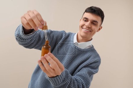 Young man with bottle of CBD oil on light background