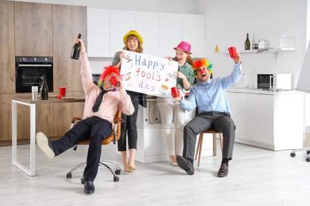 Foto de Gente de negocios con póster y bebidas celebrando el Día de los Inocentes en la cocina en la fiesta de oficina - Imagen libre de derechos
