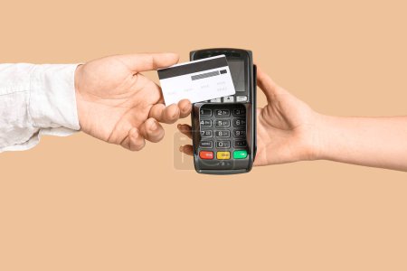Male hand with credit card and payment terminal on beige background