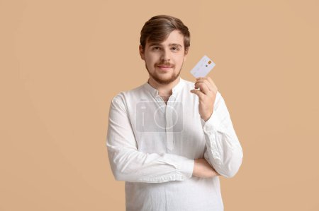 Young man with credit card on beige background