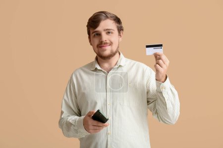 Young man with credit card and mobile phone on beige background