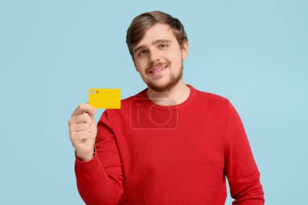 Lächelnder junger Mann mit Kreditkarte auf blauem Hintergrund