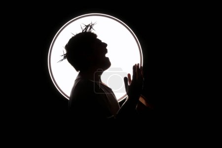 Silhouette d'homme en Jésus robe et couronne d'épines criant sur fond noir